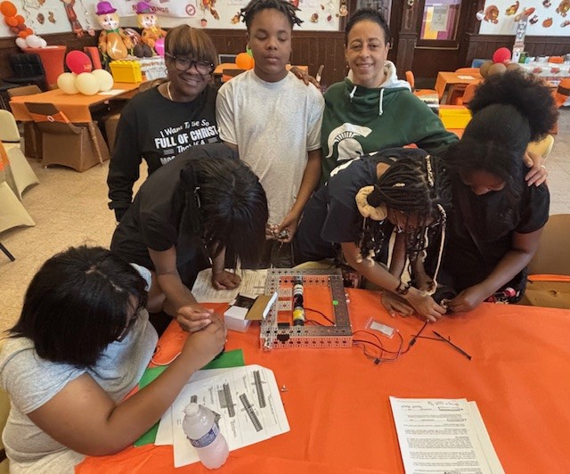  students stand with teacher in front of robotics table