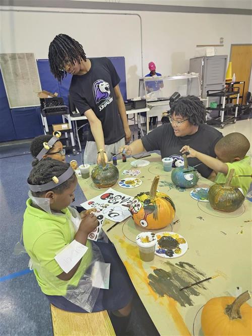  Students sitting around lunch tables painting pumpkins