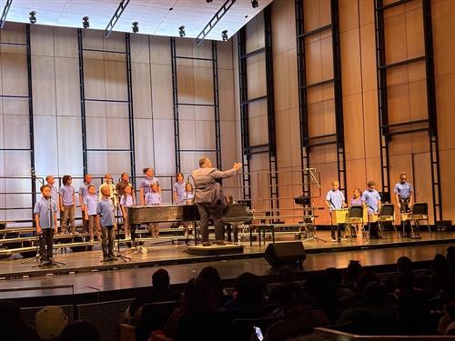 students playing instruments standing on choir raisers conductor conducting