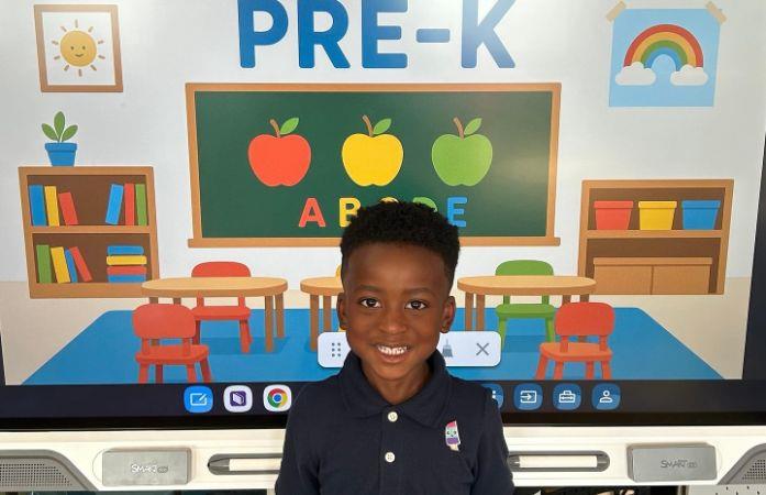  student standing in front of welcome to prek sign