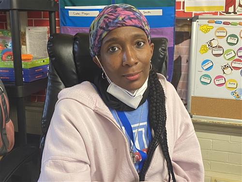 Teacher wearing pink purple scarf on her head with a pink top.