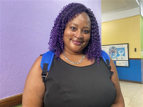 Teacher wearing a dark top with necklace and smiling