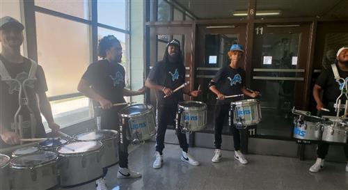 5 men standing with drums playing them in a hallway by a door