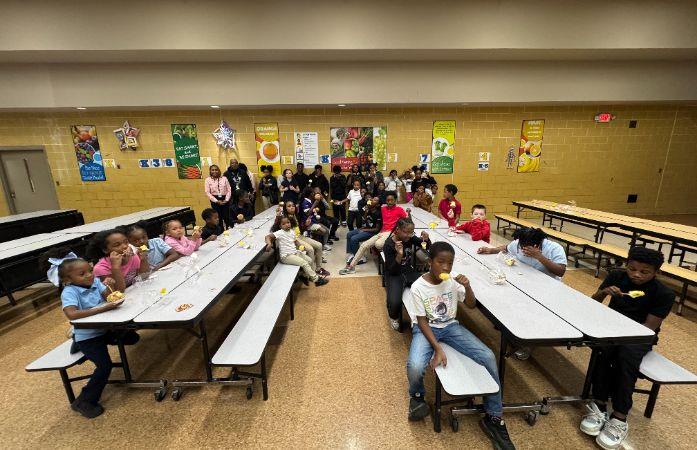  students in a lunchroom, sitting at lunch tables. 