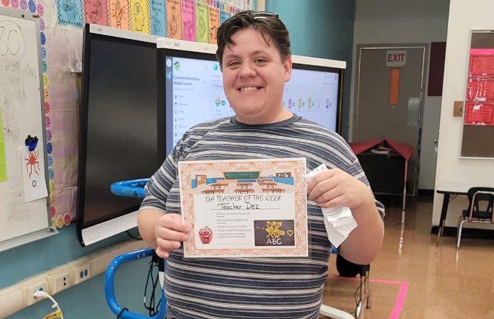  Teacher holding a certificate in a classroom.