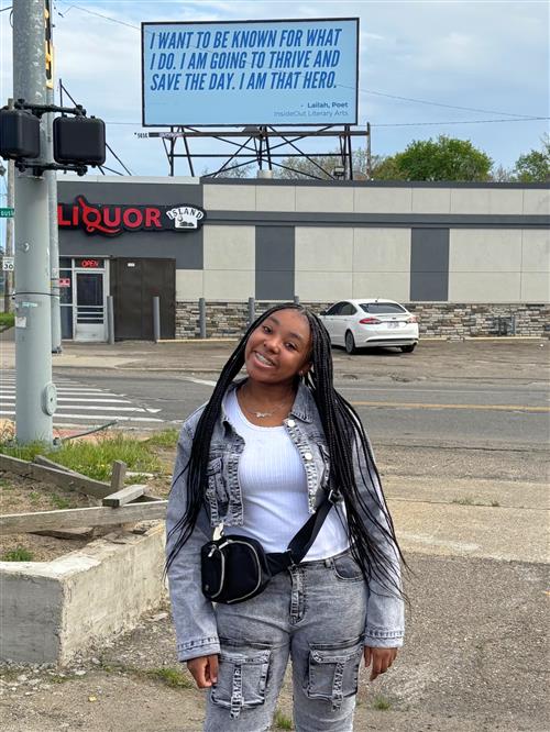   A young girl standing outside in front of a billboard. 