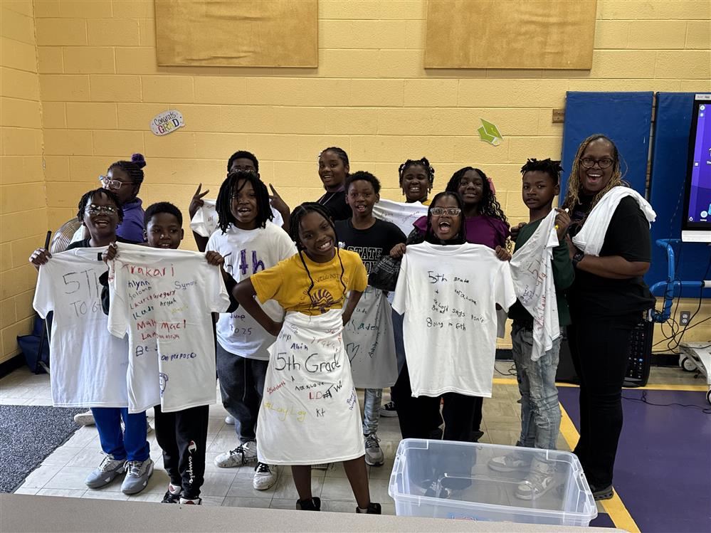  Students standing with white shirts with their names on them.