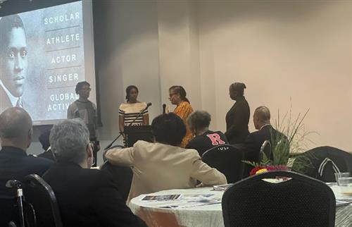 A boy and 3 ladies standing with a person speaking with the microphone.