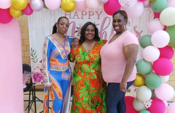 Three Ladies standing in front of a Mother's day backdrop