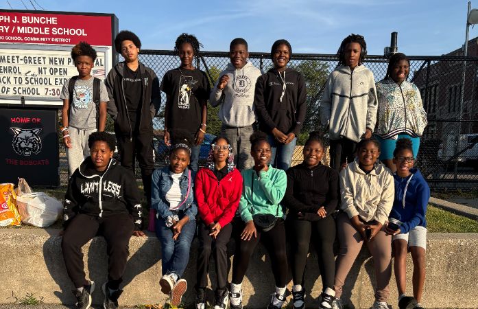 Boys and Girls smiling for the camera in front of a school sign