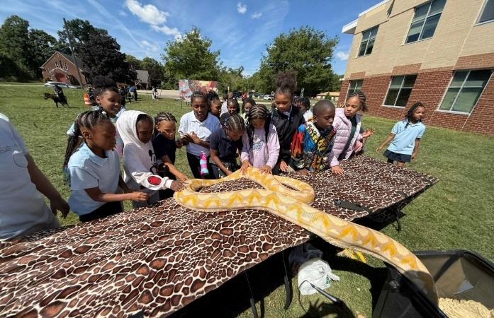  Students standing around table observing a yellow python